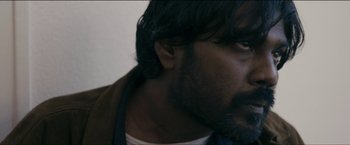Movie still from “Dheepan” (2015), directed by Jacques Audiard – A person with long hair and a beard; Close Up shot, Low angle
