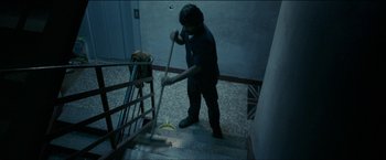Movie still from “Dheepan” (2015), directed by Jacques Audiard – A man is sweeping the stairs with a banana peel; Wide shot, Overhead angle