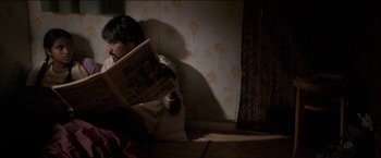 Movie still from “Dheepan” (2015), directed by Jacques Audiard – A man sitting on the floor reading a newspaper; Medium shot, High angle