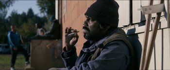 Movie still from “Dheepan” (2015), directed by Jacques Audiard – A man sitting outside with a cigarette in his mouth; Medium shot, Over the shoulder angle