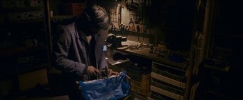 Movie still from “Dheepan” (2015), directed by Jacques Audiard – A man is working in a workshop with a blue bag; Medium shot, High angle