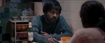 Movie still from “Dheepan” (2015), directed by Jacques Audiard – A man sitting at a table with a bottle of beer; Medium shot, Over the shoulder angle