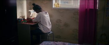 Movie still from “Dheepan” (2015), directed by Jacques Audiard – A woman sitting at a table in front of an open window; Medium shot, High angle