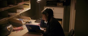 Movie still from “Dheepan” (2015), directed by Jacques Audiard – A woman sitting at a table using a tablet computer; Medium shot, High angle
