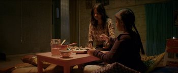 Movie still from “Dheepan” (2015), directed by Jacques Audiard – Two women are sitting at a table and one of the women is holding a spoon; Medium shot, High angle