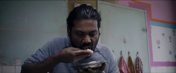 Movie still from “Dheepan” (2015), directed by Jacques Audiard – A man eating a piece of cake while holding a plate; Close Up shot, Low angle