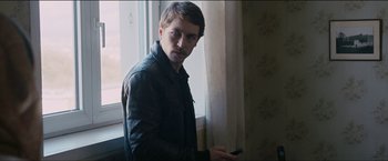 Movie still from “Dheepan” (2015), directed by Jacques Audiard – A man holding a cell phone in front of a window; Medium shot, Over the shoulder angle