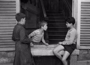 Movie still from “Diabolique” (1955), directed by Henri-Georges Clouzot – Three young boys are sitting on the steps of an old house; Wide shot, High angle