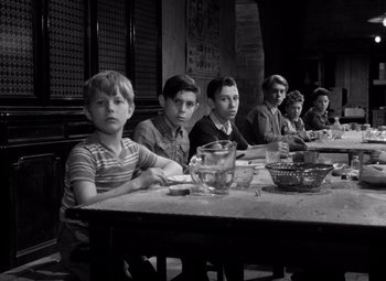 Movie still from “Diabolique” (1955), directed by Henri-Georges Clouzot – A black and white photo of a group of young men sitting at a table; Medium shot, High angle