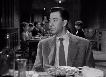 Movie still from “Diabolique” (1955), directed by Henri-Georges Clouzot – A man sitting at a table with a plate in front of him; Medium shot, Over the shoulder angle