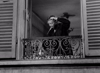 Movie still from “Diabolique” (1955), directed by Henri-Georges Clouzot – A man standing on a balcony smoking a cigarette; Medium shot, Low angle