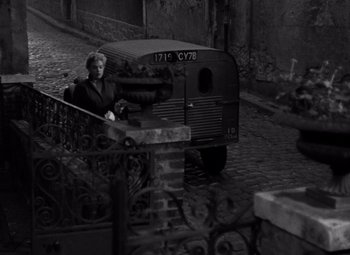 Movie still from “Diabolique” (1955), directed by Henri-Georges Clouzot – A man sitting in front of a bus on a street; Wide shot, High angle
