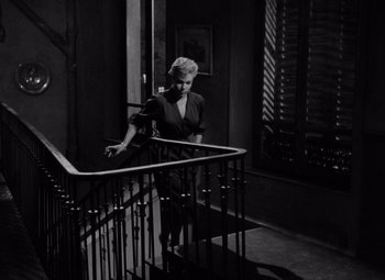 Movie still from “Diabolique” (1955), directed by Henri-Georges Clouzot – A black and white photo of a woman standing on top of a staircase railing; Wide shot, High angle