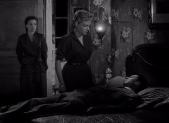 Movie still from “Diabolique” (1955), directed by Henri-Georges Clouzot – A woman standing next to a man laying in a bed; Wide shot, High angle