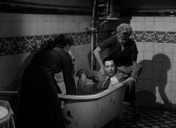 Movie still from “Diabolique” (1955), directed by Henri-Georges Clouzot – A man is in a bathtub while two women watch; Wide shot, High angle