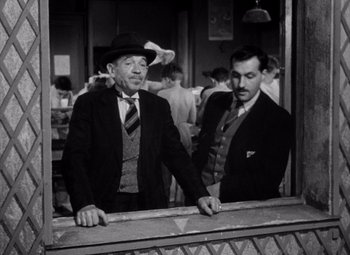 Movie still from “Diabolique” (1955), directed by Henri-Georges Clouzot – Two men standing next to each other in front of a building; Medium shot, Over the shoulder angle