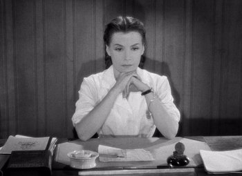 Movie still from “Diabolique” (1955), directed by Henri-Georges Clouzot – A black and white photo of a woman sitting at a desk; Medium shot, High angle