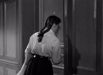 Movie still from “Diabolique” (1955), directed by Henri-Georges Clouzot – A woman with a long braid standing in front of a door; Medium shot, Over the shoulder angle