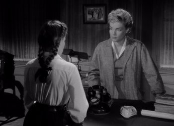 Movie still from “Diabolique” (1955), directed by Henri-Georges Clouzot – A woman is looking in the mirror while a woman in a dress is looking at her; Medium shot, High angle