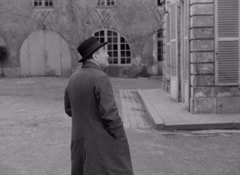 Movie still from “Diabolique” (1955), directed by Henri-Georges Clouzot – An older man wearing a coat and a hat; Medium shot, High angle