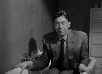 Movie still from “Diabolique” (1955), directed by Henri-Georges Clouzot – A black and white photo of a man sitting on a toilet; Medium shot, Low angle