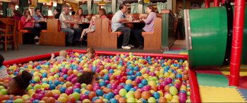 Movie still from “Diary of a Wimpy Kid: The Long Haul” (2017), directed by David Bowers – Two adults and a child sitting at a table in a ball pit; Wide shot, High angle