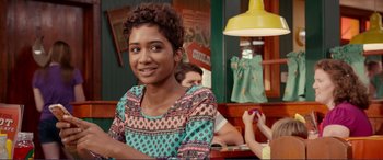 Movie still from “Diary of a Wimpy Kid: The Long Haul” (2017), directed by David Bowers – A woman sitting at a table in front of a yellow lamp; Close Up shot, Over the shoulder angle