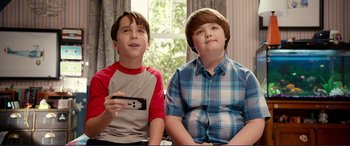 Movie still from “Diary of a Wimpy Kid: The Long Haul” (2017), directed by David Bowers – Two young boys sitting next to each other holding a game controller; Medium shot, High angle