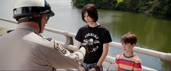 Movie still from “Diary of a Wimpy Kid: The Long Haul” (2017), directed by David Bowers – A man is handing a woman something from a bridge; Medium shot, Over the shoulder angle