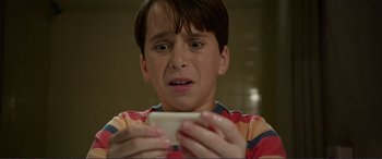 Movie still from “Diary of a Wimpy Kid: The Long Haul” (2017), directed by David Bowers – A young boy holding a cell phone in his hands; Close Up shot, Low angle