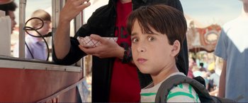 Movie still from “Diary of a Wimpy Kid: The Long Haul” (2017), directed by David Bowers – A young boy is looking into the camera while a man holds a paper cup in front of him; Close Up shot, Over the shoulder angle