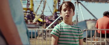 Movie still from “Diary of a Wimpy Kid: The Long Haul” (2017), directed by David Bowers – A young boy standing in front of an amusement park ride; Medium shot, Over the shoulder angle