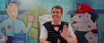Movie still from “Diary of a Wimpy Kid: The Long Haul” (2017), directed by David Bowers – A man wearing a red bow tie waving; Medium shot, Over the shoulder angle