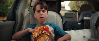 Movie still from “Diary of a Wimpy Kid: The Long Haul” (2017), directed by David Bowers – A boy sitting in the back seat of a car holding a bag of cheetos; Close Up shot, Over the shoulder angle