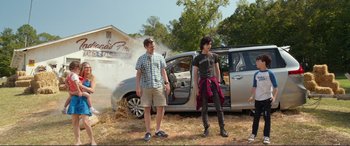 Movie still from “Diary of a Wimpy Kid: The Long Haul” (2017), directed by David Bowers – Two people standing next to a car in front of a building; Wide shot, Over the shoulder angle