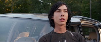Movie still from “Diary of a Wimpy Kid: The Long Haul” (2017), directed by David Bowers – A man with long black hair standing in front of a car; Close Up shot, Over the shoulder angle