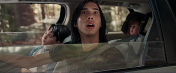 Movie still from “Diary of a Wimpy Kid: The Long Haul” (2017), directed by David Bowers – A man with long black hair driving in a car; Close Up shot, Over the shoulder angle