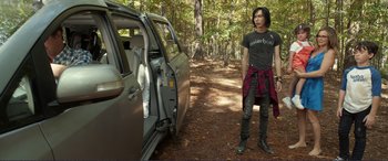 Movie still from “Diary of a Wimpy Kid: The Long Haul” (2017), directed by David Bowers – A man standing in front of a parked car; Medium shot, Over the shoulder angle