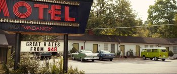 Movie still from “Diary of a Wimpy Kid: The Long Haul” (2017), directed by David Bowers – Cars parked in front of a motel with a neon motel sign; Wide shot, High angle