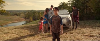 Movie still from “Diary of a Wimpy Kid: The Long Haul” (2017), directed by David Bowers – A young boy standing in front of a parked car; Wide shot, Over the shoulder angle