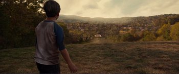 Movie still from “Diary of a Wimpy Kid: The Long Haul” (2017), directed by David Bowers – A man standing on top of a grass covered field; Wide shot, High angle