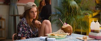 Movie still from “Do Revenge” (2022), directed by Jennifer Kaytin Robinson – A woman sitting at a table with a plate of food; Medium shot, Over the shoulder angle