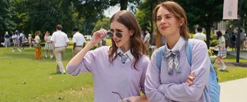 Movie still from “Do Revenge” (2022), directed by Jennifer Kaytin Robinson – Two young women are standing in a park and one of them is talking on a cell phone; Medium shot, Over the shoulder angle