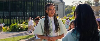 Movie still from “Do Revenge” (2022), directed by Jennifer Kaytin Robinson – A girl with long dreadlocks standing in front of a group of people; Medium shot, Low angle