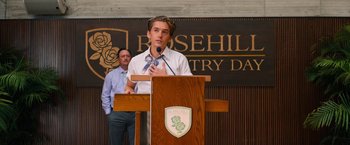 Movie still from “Do Revenge” (2022), directed by Jennifer Kaytin Robinson – A man standing at a podium speaking to a crowd; Medium shot, Low angle