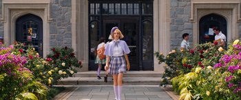 Movie still from “Do Revenge” (2022), directed by Jennifer Kaytin Robinson – A woman in a purple outfit standing in front of a building; Wide shot, Low angle