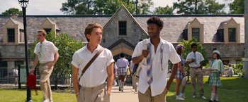 Movie still from “Do Revenge” (2022), directed by Jennifer Kaytin Robinson – Two young men walking down a sidewalk in front of a building; Medium shot, Low angle