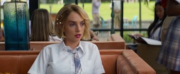 Movie still from “Do Revenge” (2022), directed by Jennifer Kaytin Robinson – A woman sitting on top of a couch wearing a tie; Close Up shot, Over the shoulder angle