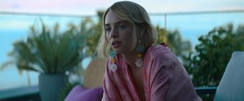 Movie still from “Do Revenge” (2022), directed by Jennifer Kaytin Robinson – A woman with blonde hair wearing a pink shirt and earrings; Close Up shot, Over the shoulder angle
