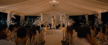 Movie still from “Do Revenge” (2022), directed by Jennifer Kaytin Robinson – A man standing in front of an audience in a white tent; Wide shot, Over the shoulder angle